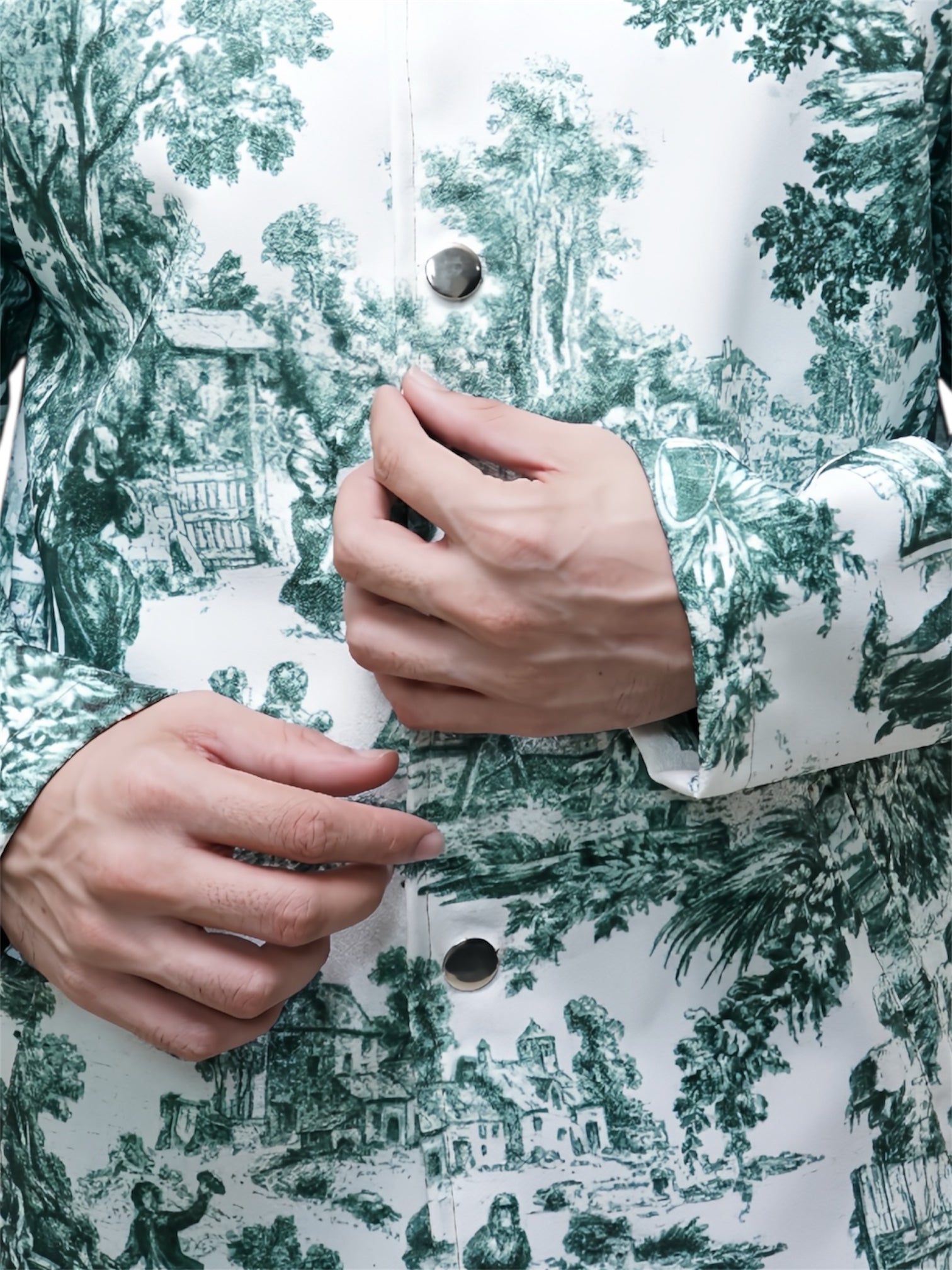 Close-up of hands buttoning a garment with a green and white patterned design.